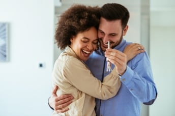 Man and woman excitedly hold keys to their house 