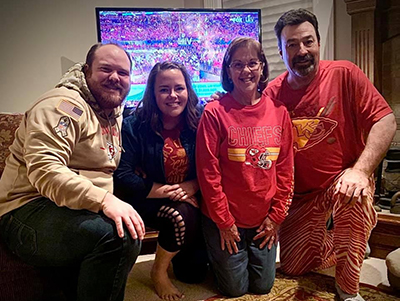 Chris Keating posing with family in front of a tv playing a Chiefs game