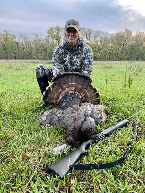 Whitney posing with wild turkey and hunting rifle.
